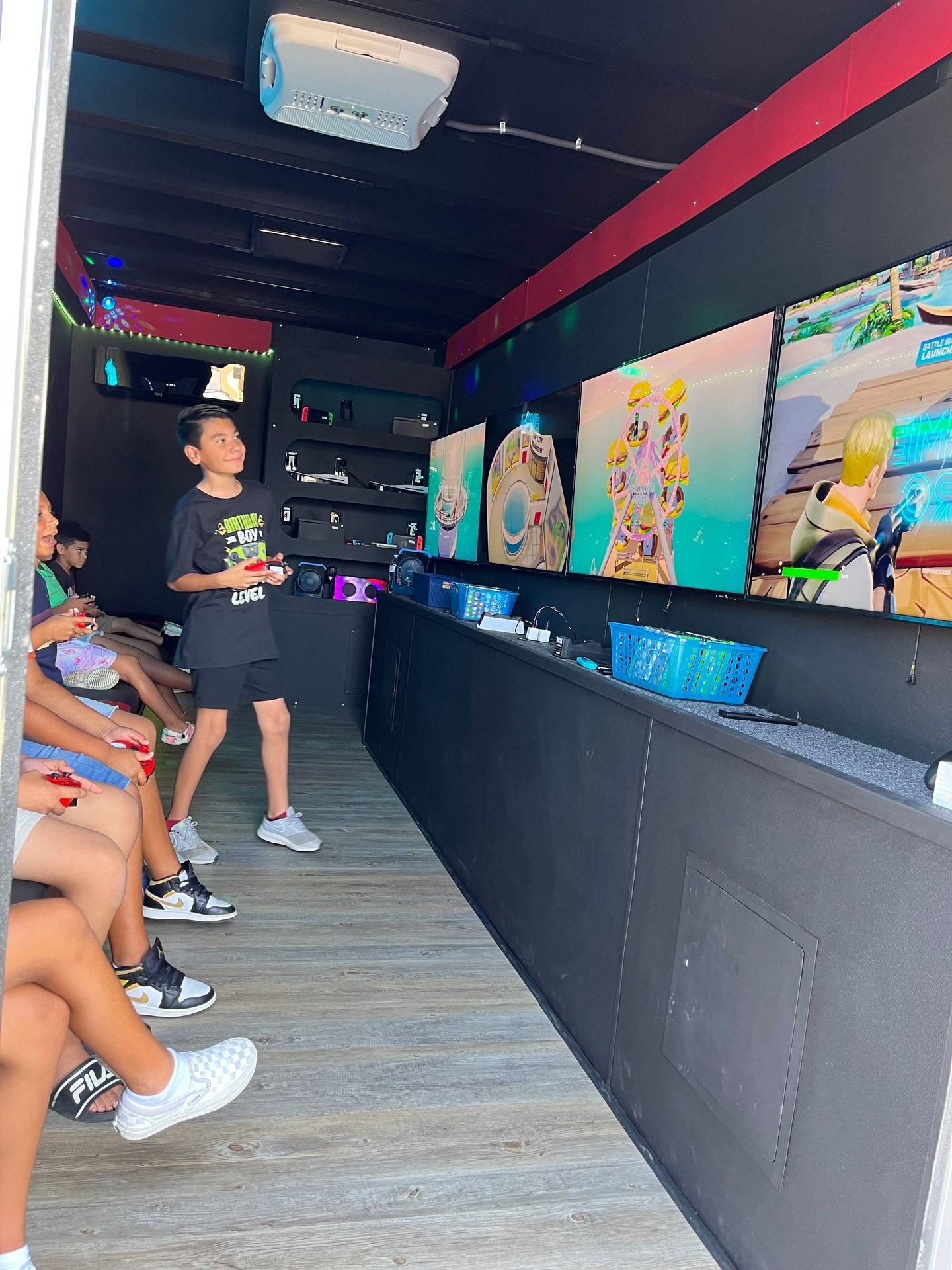 Children playing video games on multiple large screens inside a dark room with a projector on the ceiling.